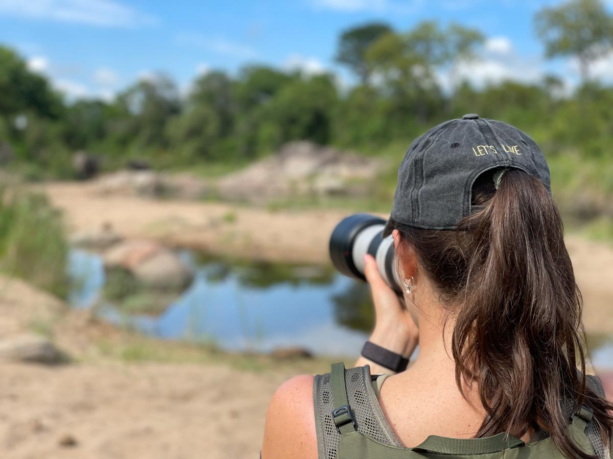A lady wearing a lets live cap taking a picture of a hippo in th edistance