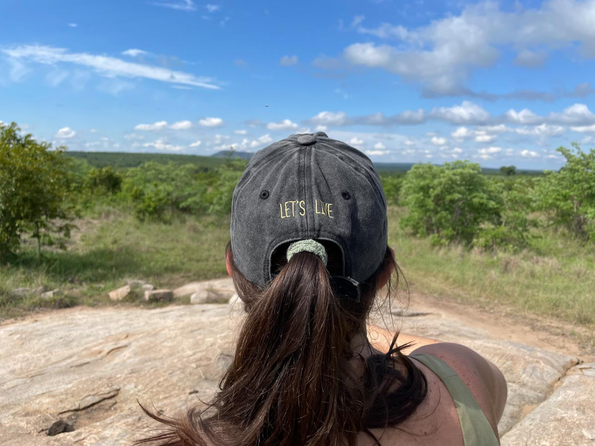 Lady wearing a lets live cap and looking into over a bushveld scene