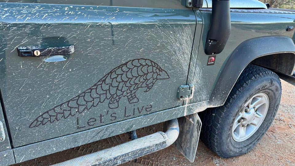 Defender with 'Let's Live' pangolin decal on a dirt road